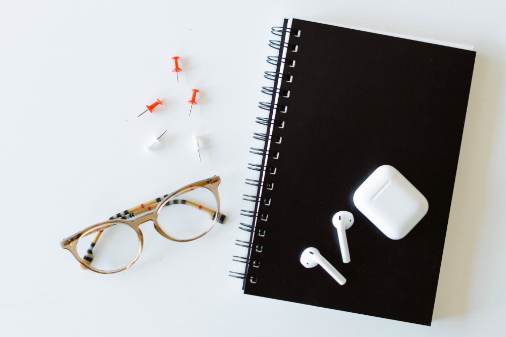 Black notebook with white earbuds and glasses on a white background